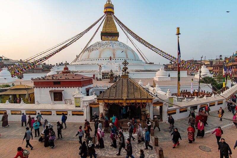 Le grand stupa blanc de Boudhanath couvert de drapeaux de prières, entouré de pèlerins et de visiteurs