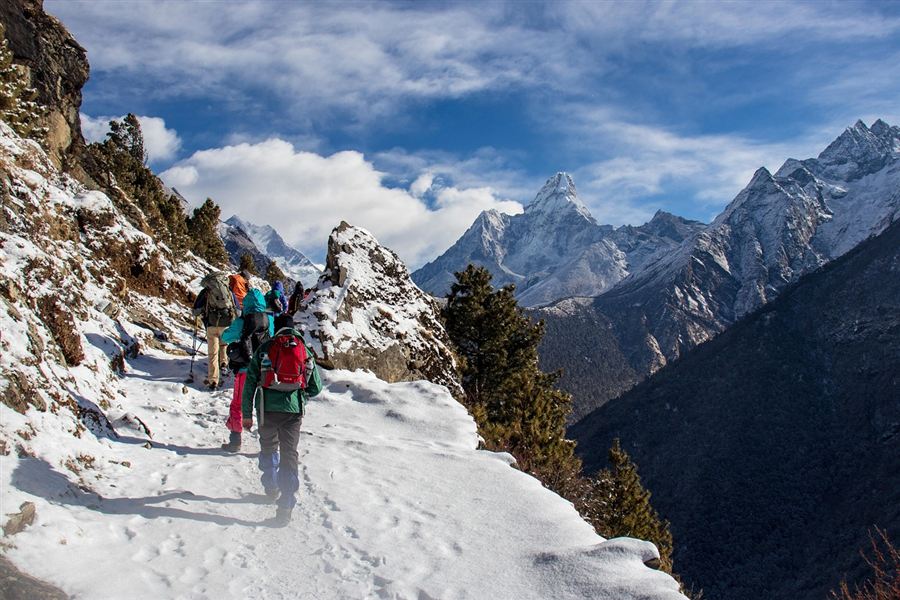 Trekkeurs avec sacs à dos sur un sentier enneigé, face à des sommets de l’Himalaya